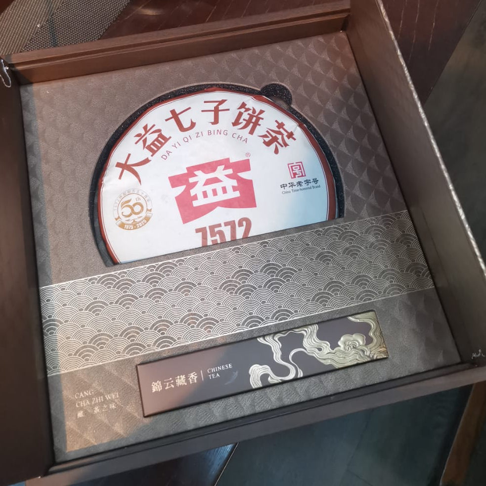 Open box containing a round product with a label, on a wooden surface.
